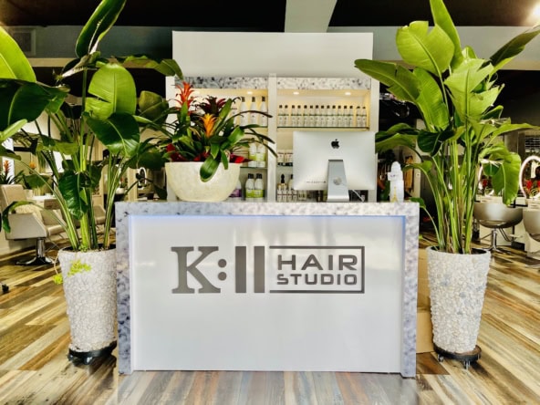 Modern salon reception area with lush green plants and a sleek white counter.