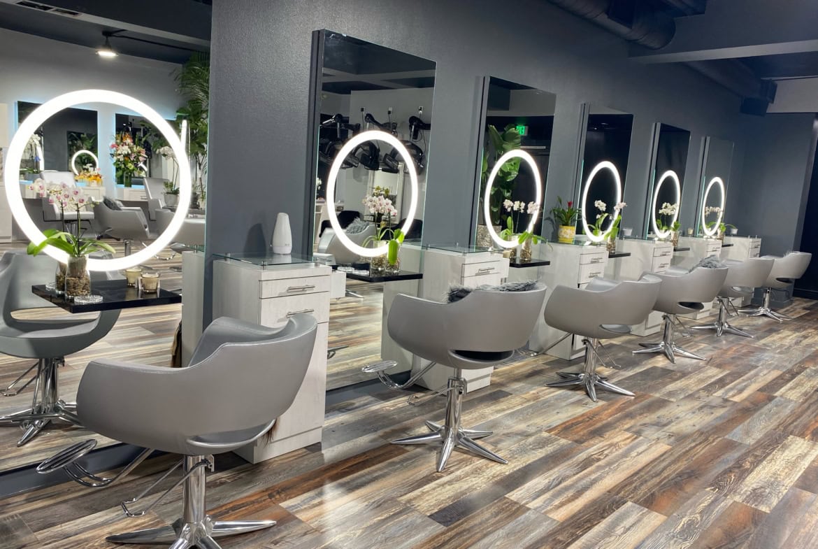 Modern salon styling stations with illuminated mirrors and comfortable chairs.