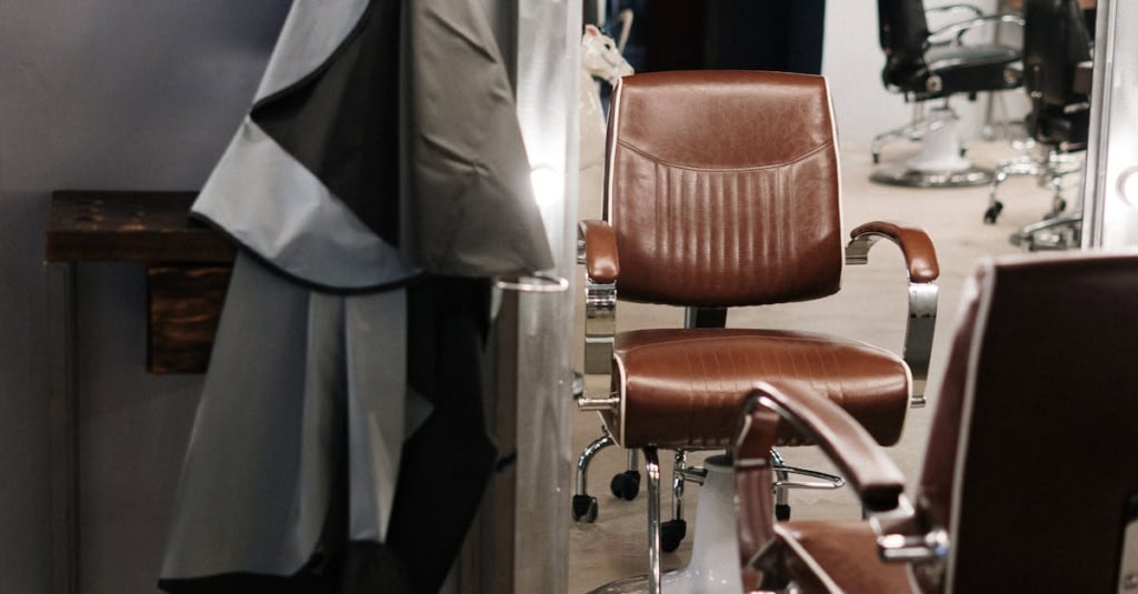 Barber chair in salon with styling cape and mirror in background.