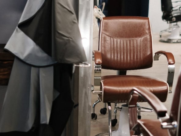 Barber chair in salon with styling cape and mirror in background.