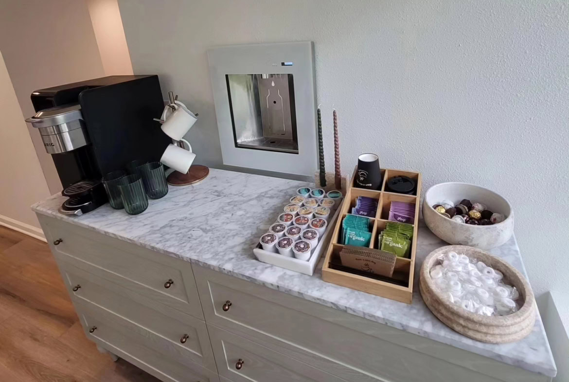 Coffee station with cups, tea, and snacks at salon break area.