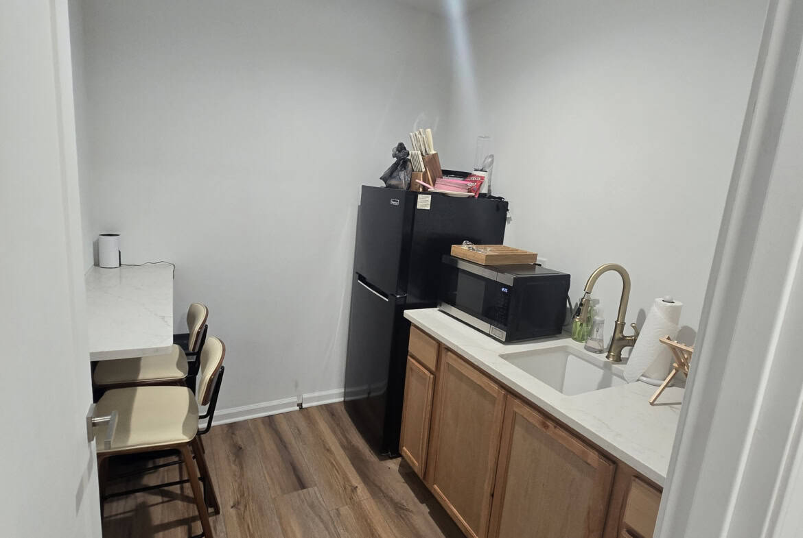 Small salon break room with kitchenette, chairs, and storage.