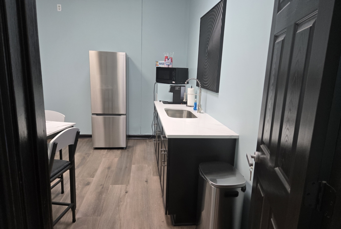 Break room with kitchenette in salon, featuring refrigerator, sink, microwave, and seating area.