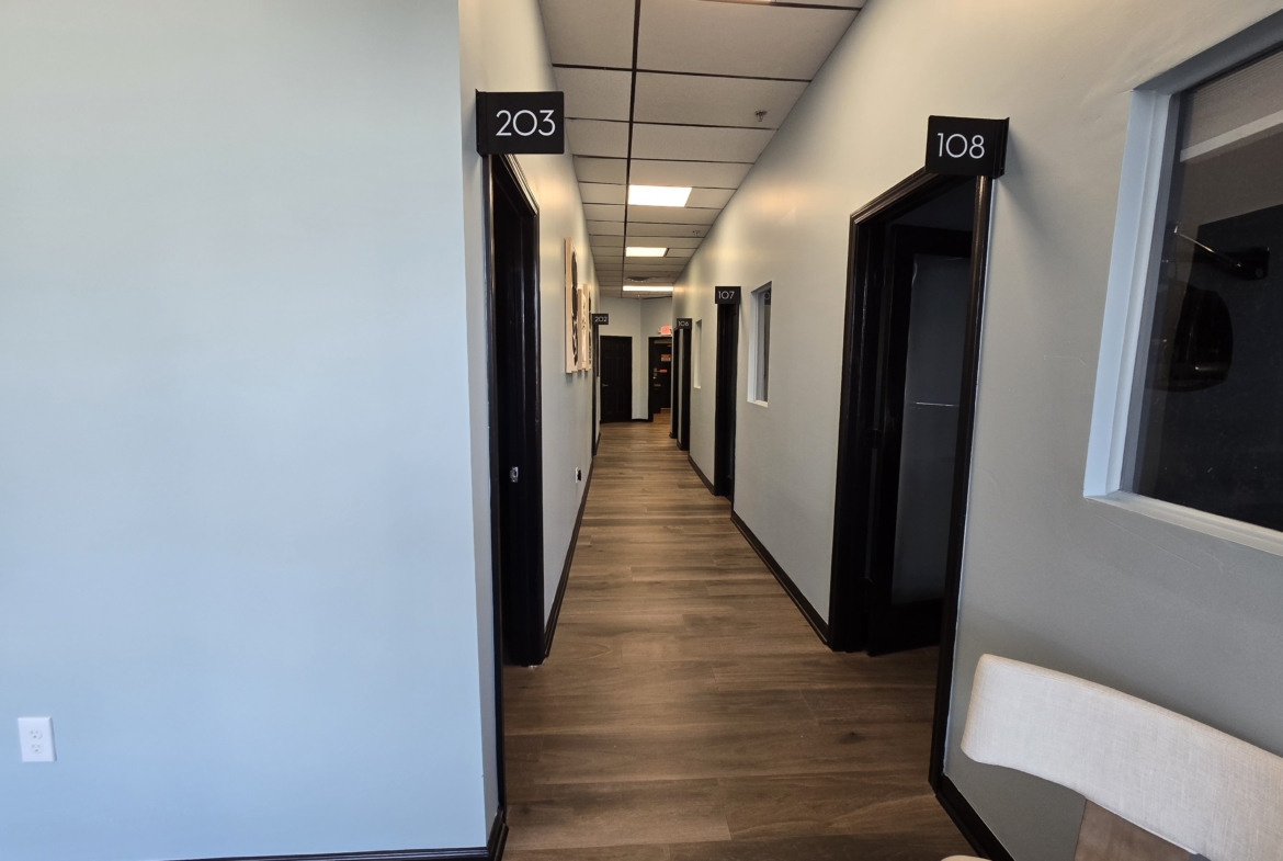 Bright salon corridor with numbered rooms 203 and 108, clean white walls, wooden flooring, and conte.