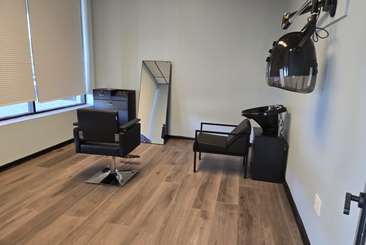 A styling station in a salon with a chair, mirror, and hair washing station for haircuts and beauty.