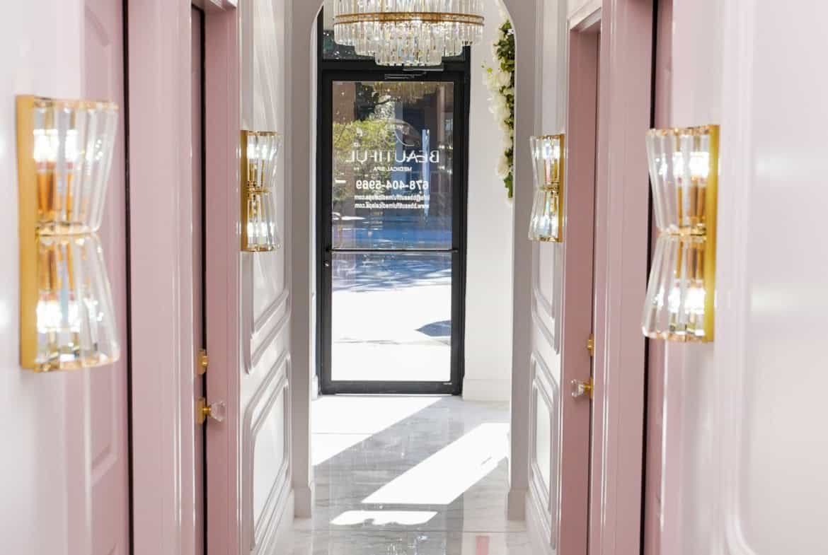 Elegant salon hallway with pink doors, crystal chandeliers, and stylish wall sconces, creating a lux.