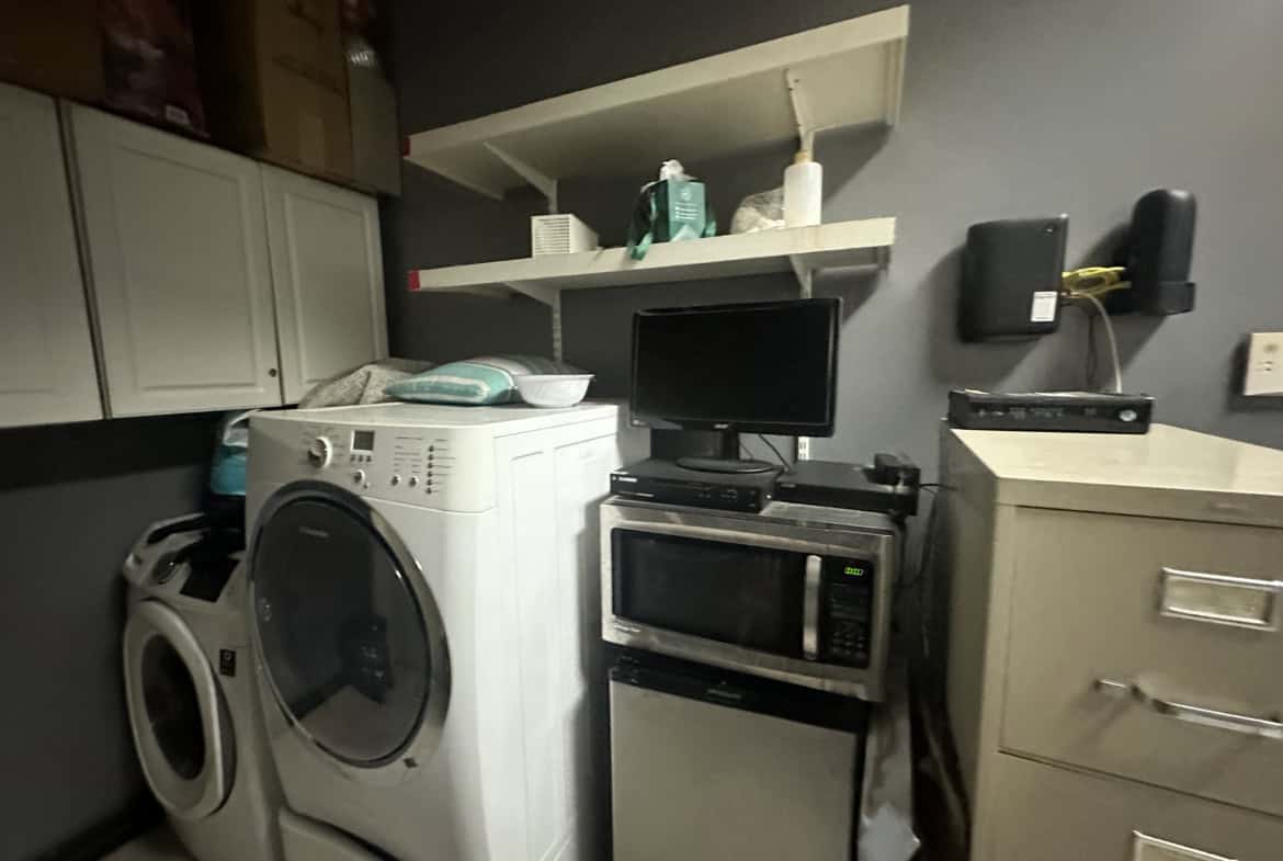 Laundry room featuring washer, dryer, microwave, and storage shelves.