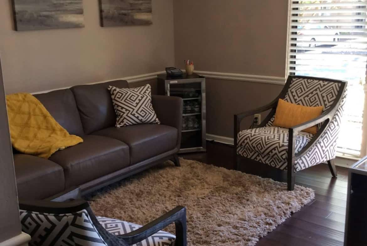 Comfortable salon waiting room with stylish chairs, artwork, and a chandelier.