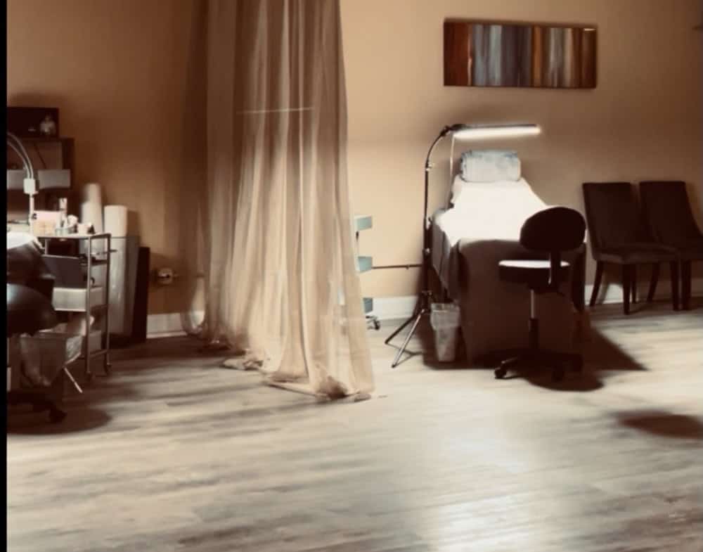 Treatment room with bed, chairs, and equipment for salon services.