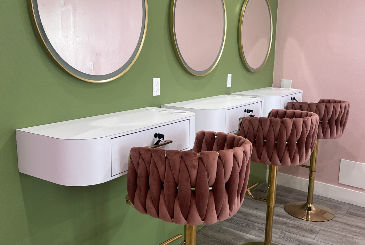 Stylish salon station with three mirrors and plush pink chairs.