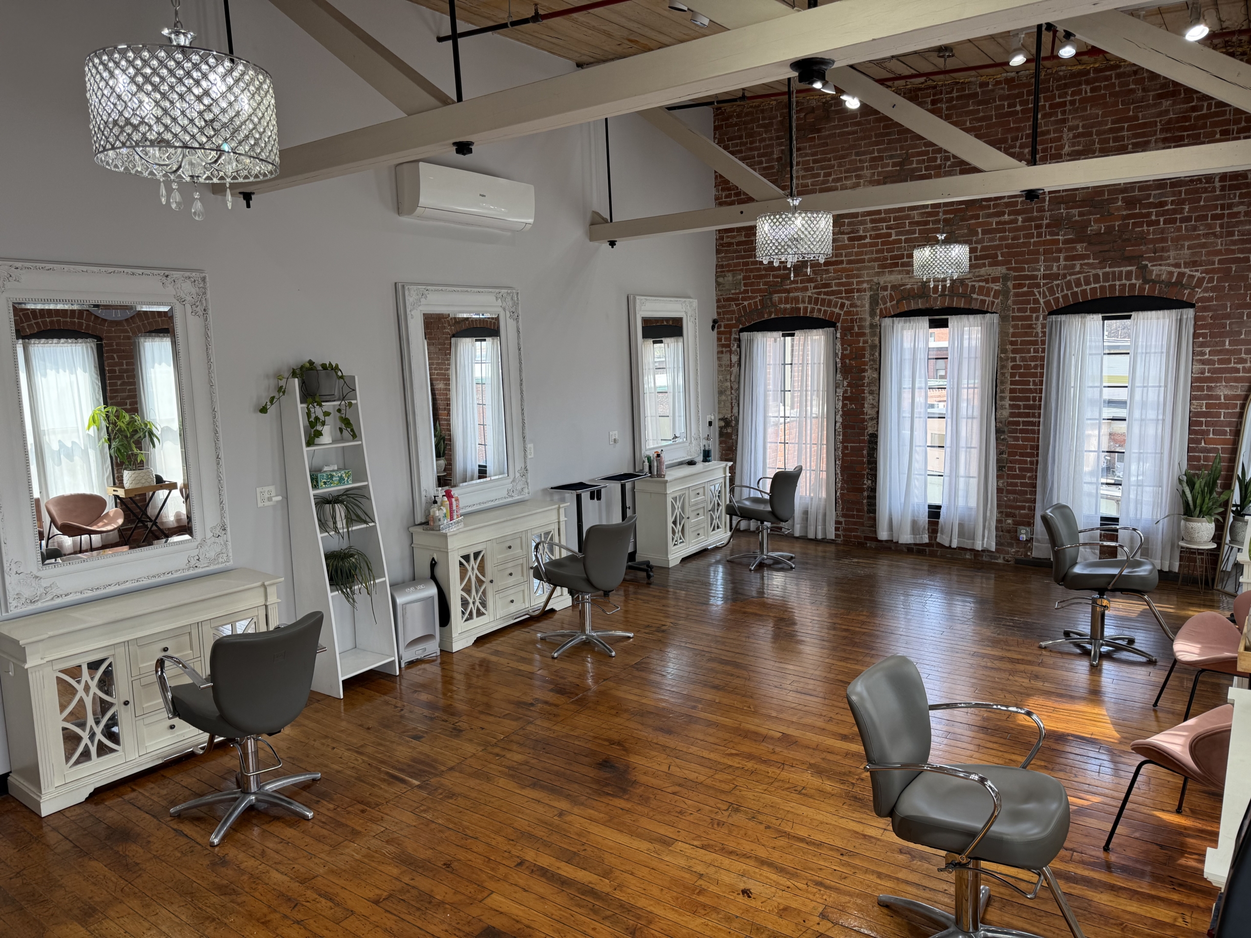 Stylish salon space with multiple styling stations, natural light, and exposed brick walls.