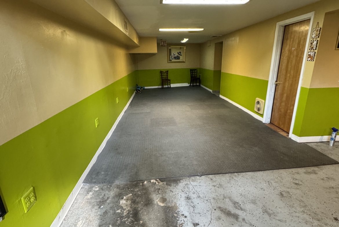 Empty salon hallway with green and beige walls, gray flooring, and seating area at the end.