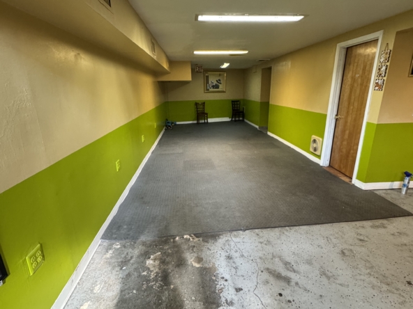 Empty salon hallway with green and beige walls, gray flooring, and seating area at the end.