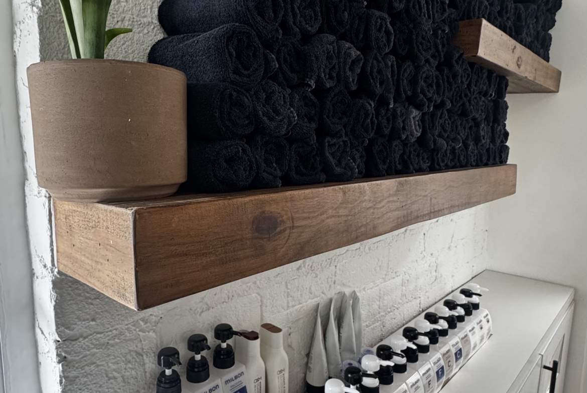 Neatly stacked black towels with salon hair care products on a white shelf.