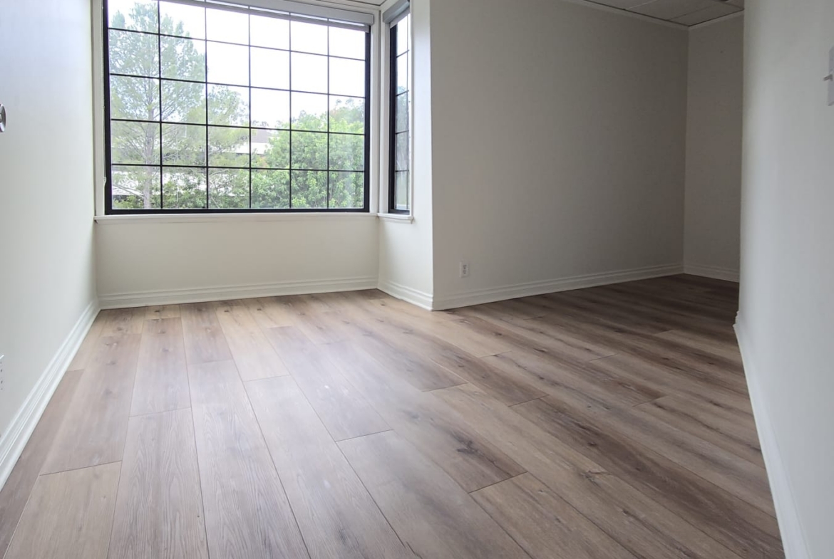Office space with large window and wooden flooring for rent or lease.