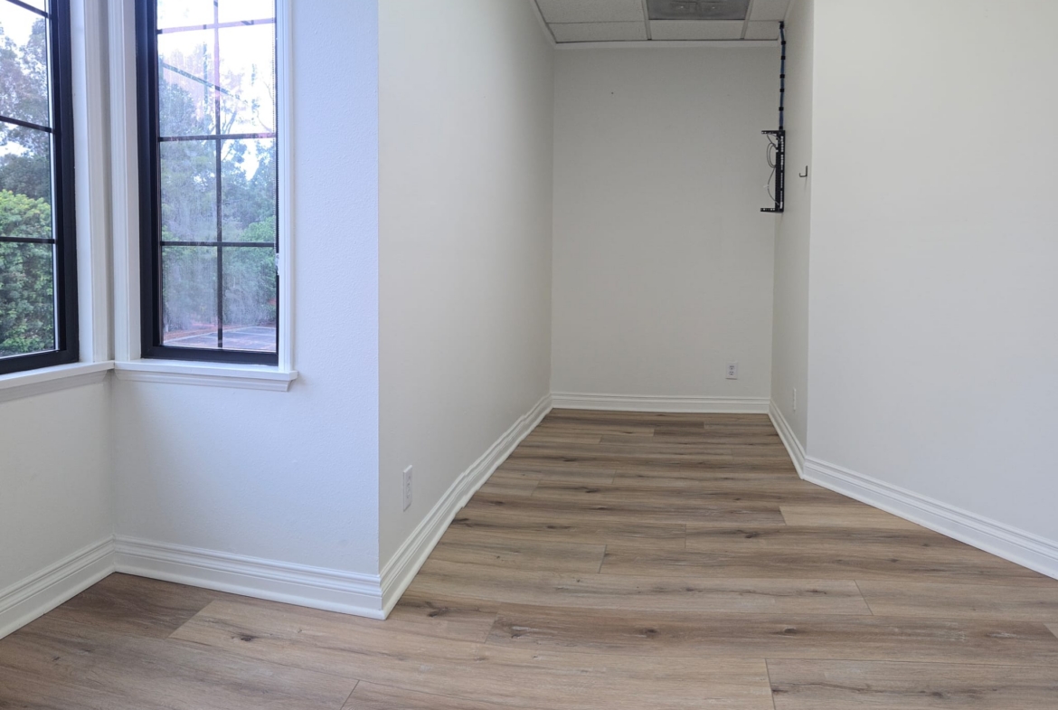 Empty salon room with large windows and hardwood flooring.