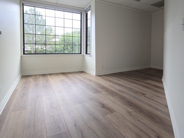 Office space with large window and wooden flooring for rent or lease.