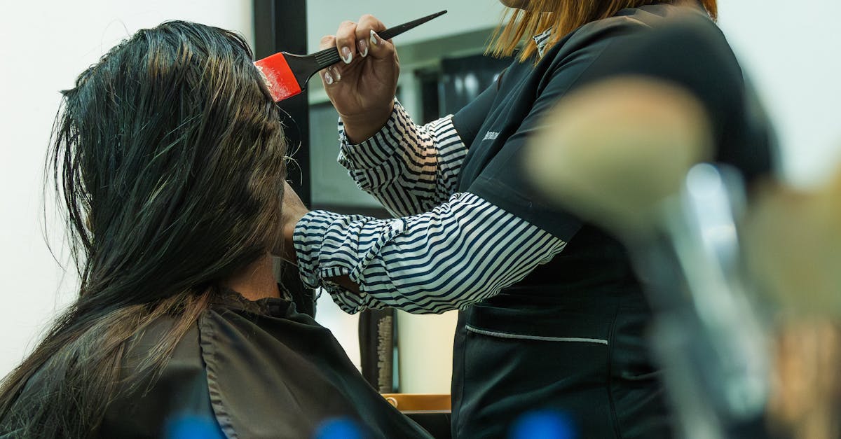Hairdresser applying color to client's hair in salon setting.