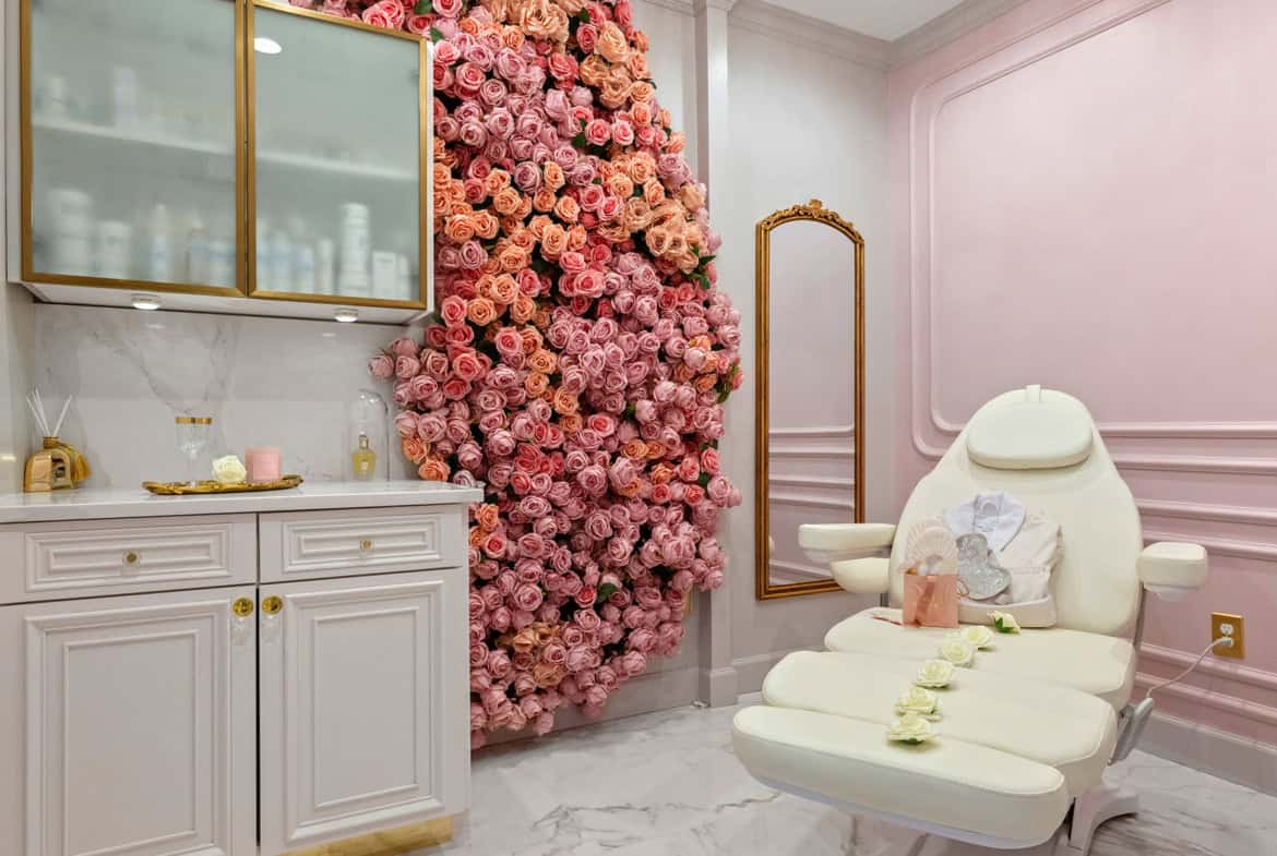 Elegant salon treatment room with pink floral wall, chandelier, and comfortable chair for client ser.