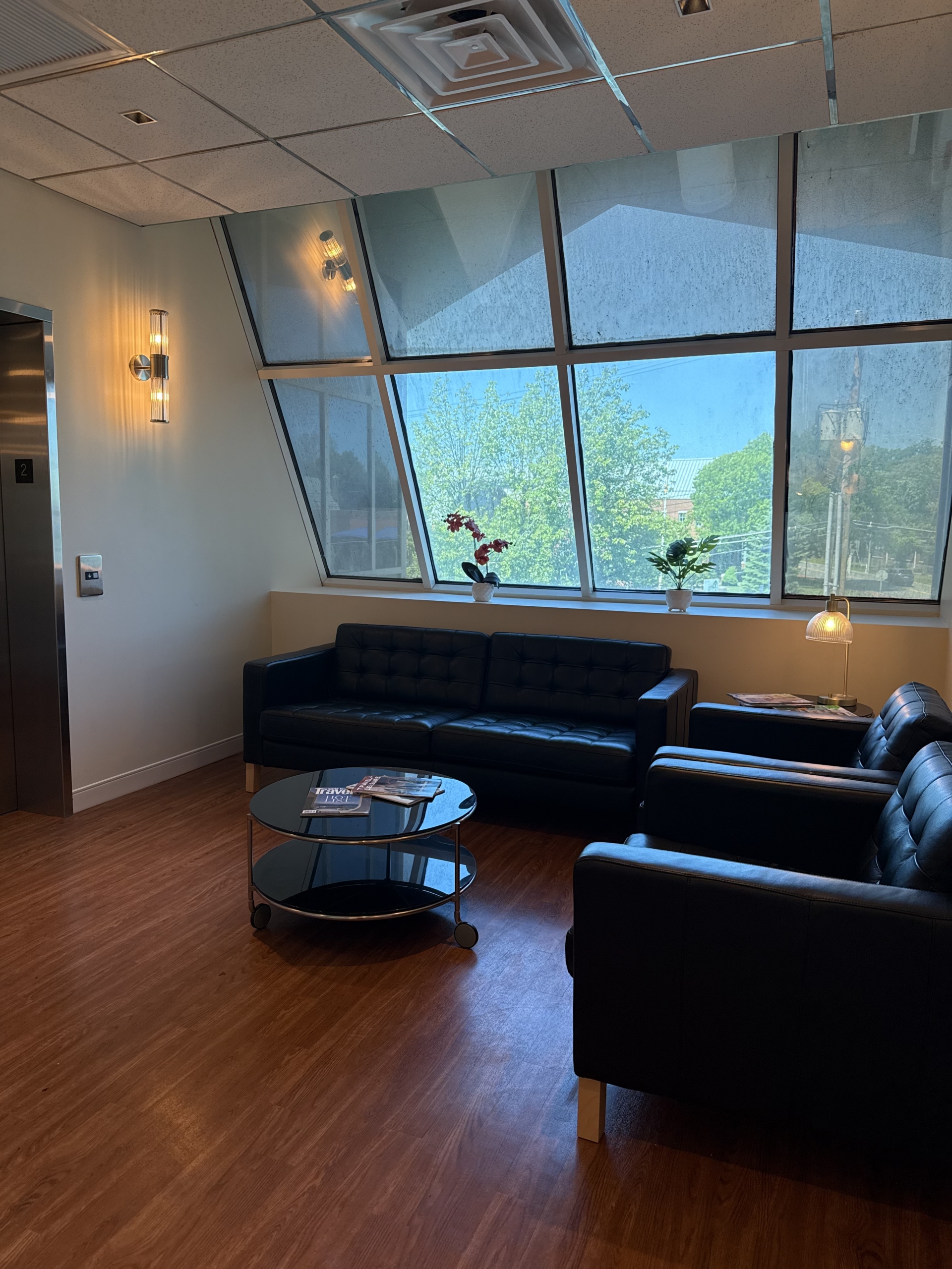 Modern salon waiting area with large windows, black leather sofas, and natural light.