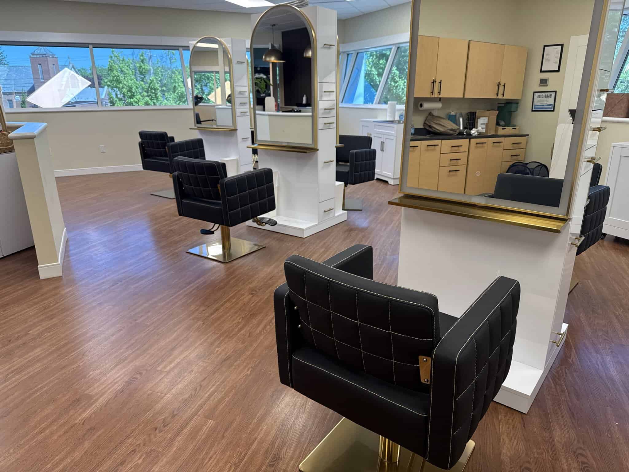 Modern salon styling stations with black chairs and large windows for natural light.