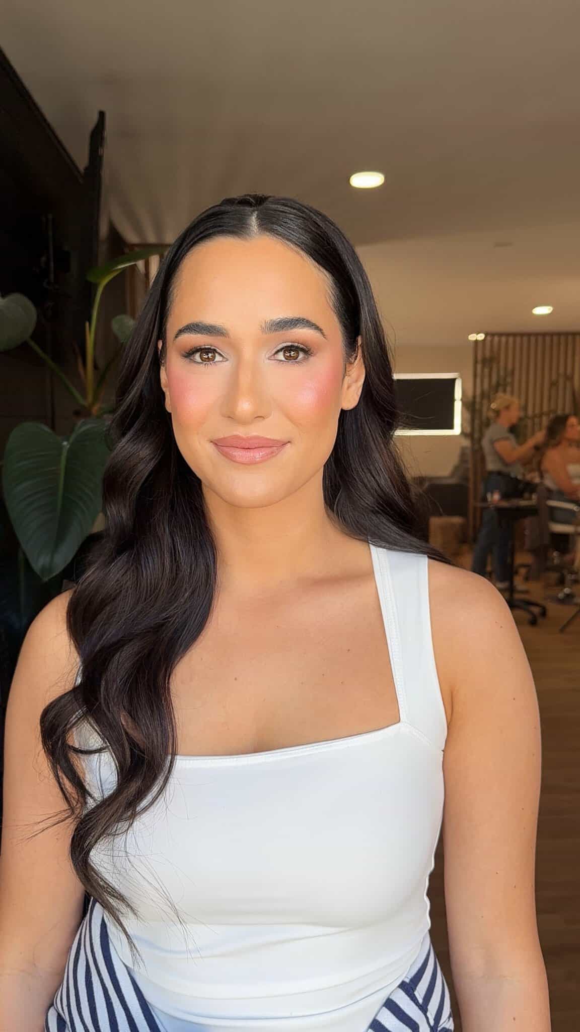 Woman with styled hair and makeup at salon, showcasing beauty services.