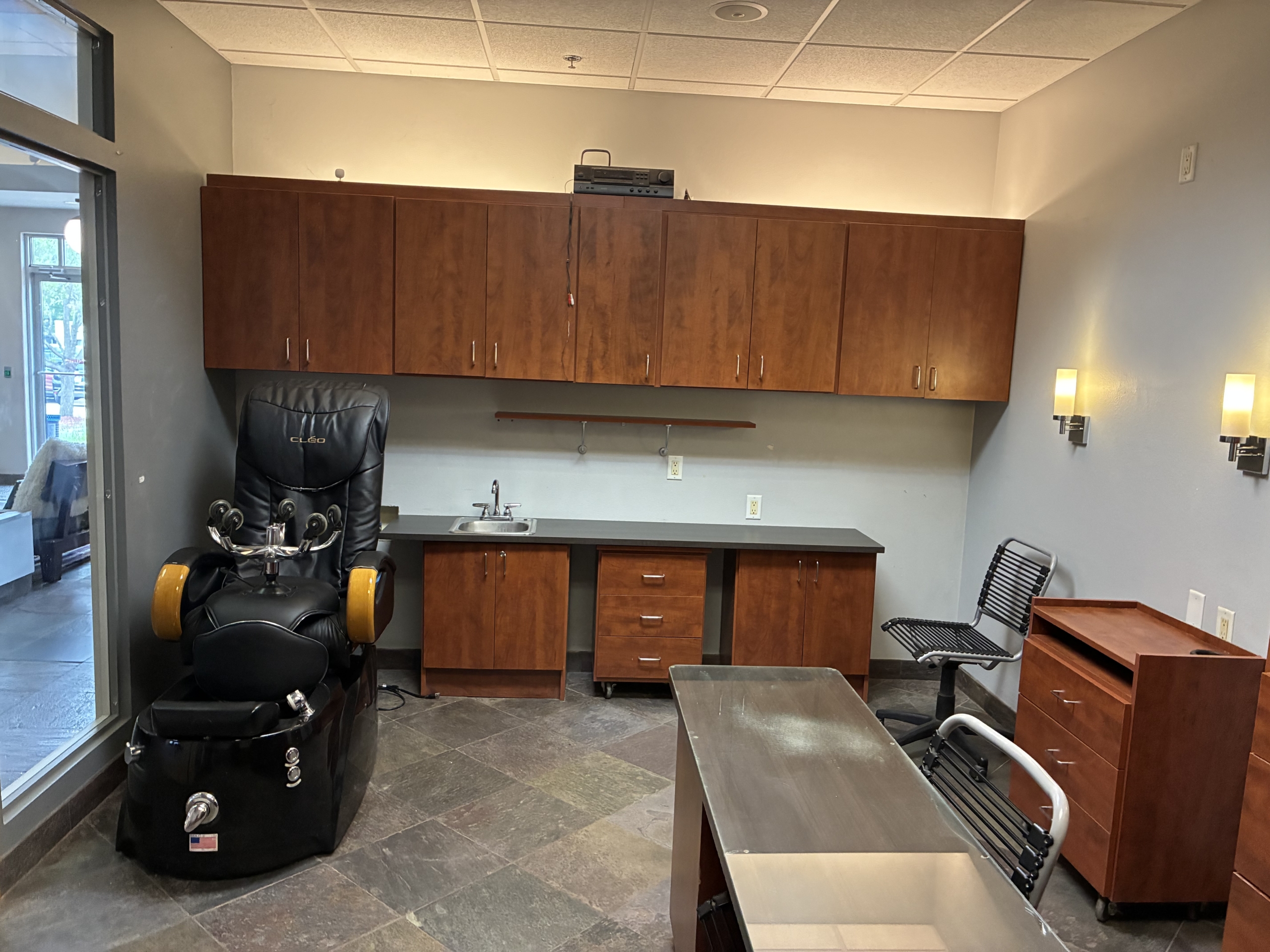 Modern salon office with massage chair, desk, and storage cabinets.