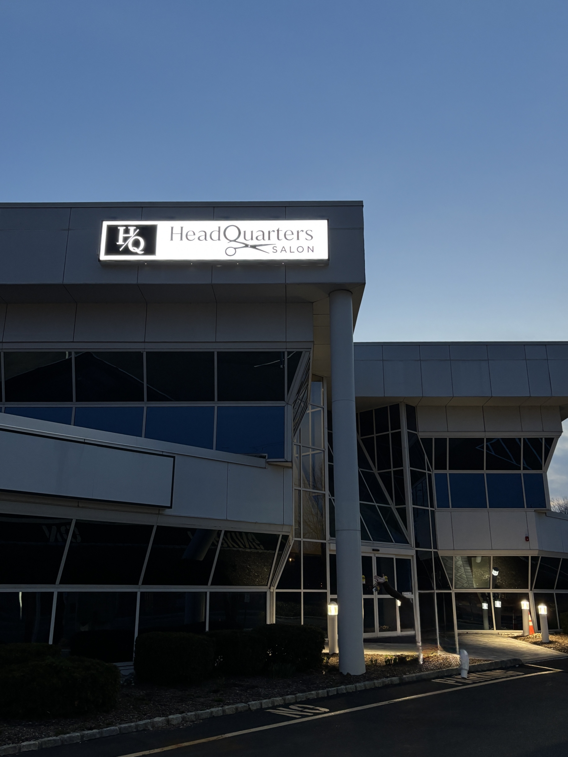 Modern HeadQuarters Salon building with glass facade and signage under clear blue sky.