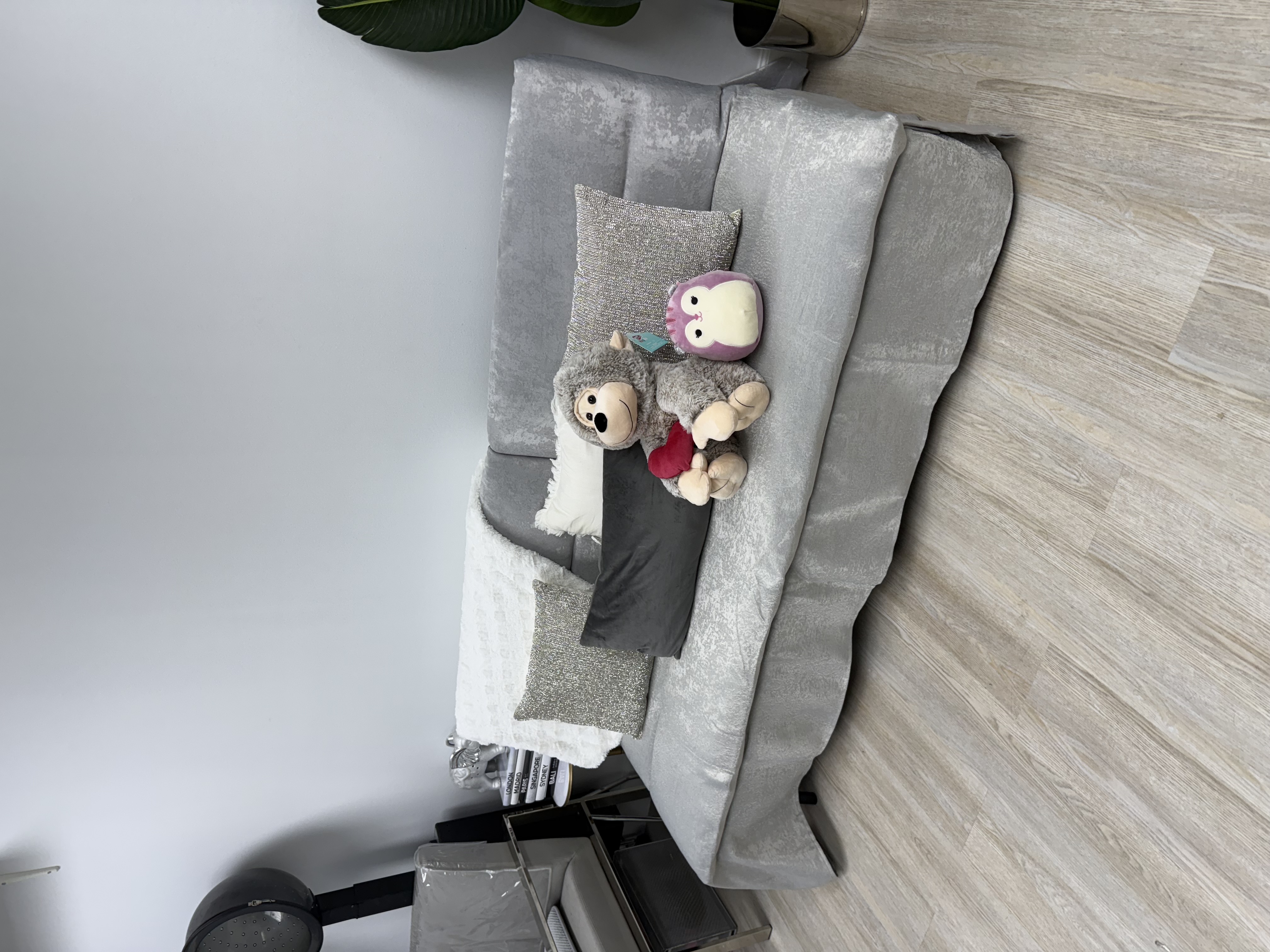 Cozy salon waiting area featuring a plush teddy bear and owl toys on a gray velvet sofa with cushion.