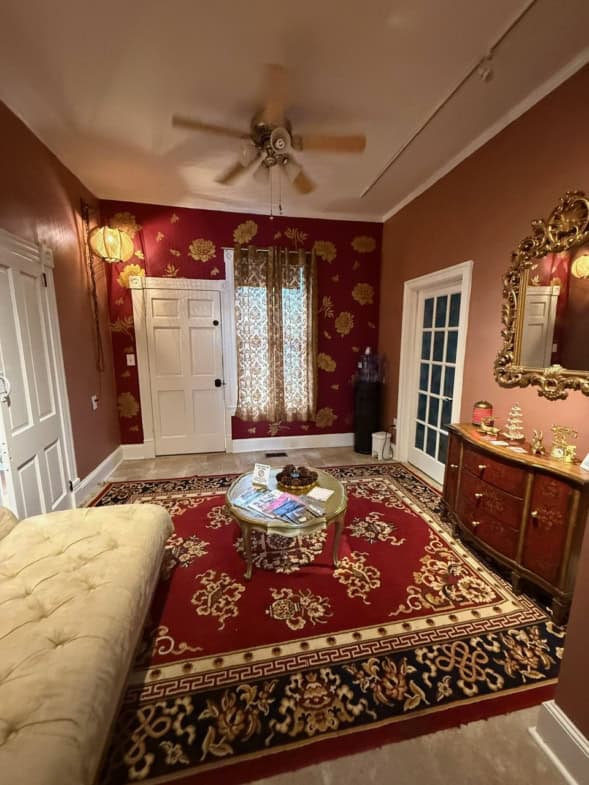 Elegant living room featuring red walls with gold floral wallpaper, a vintage rug, and classic furni.