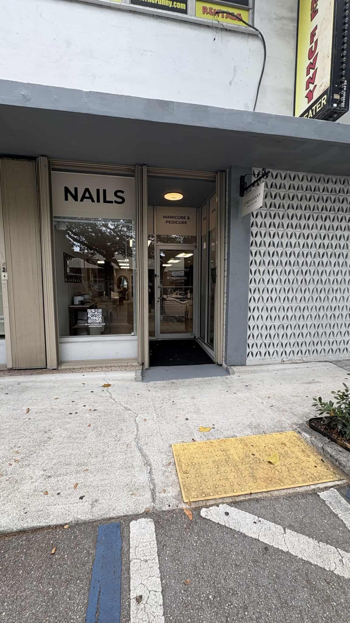 Nail salon storefront with glass door and "NAILS" sign in a commercial area.