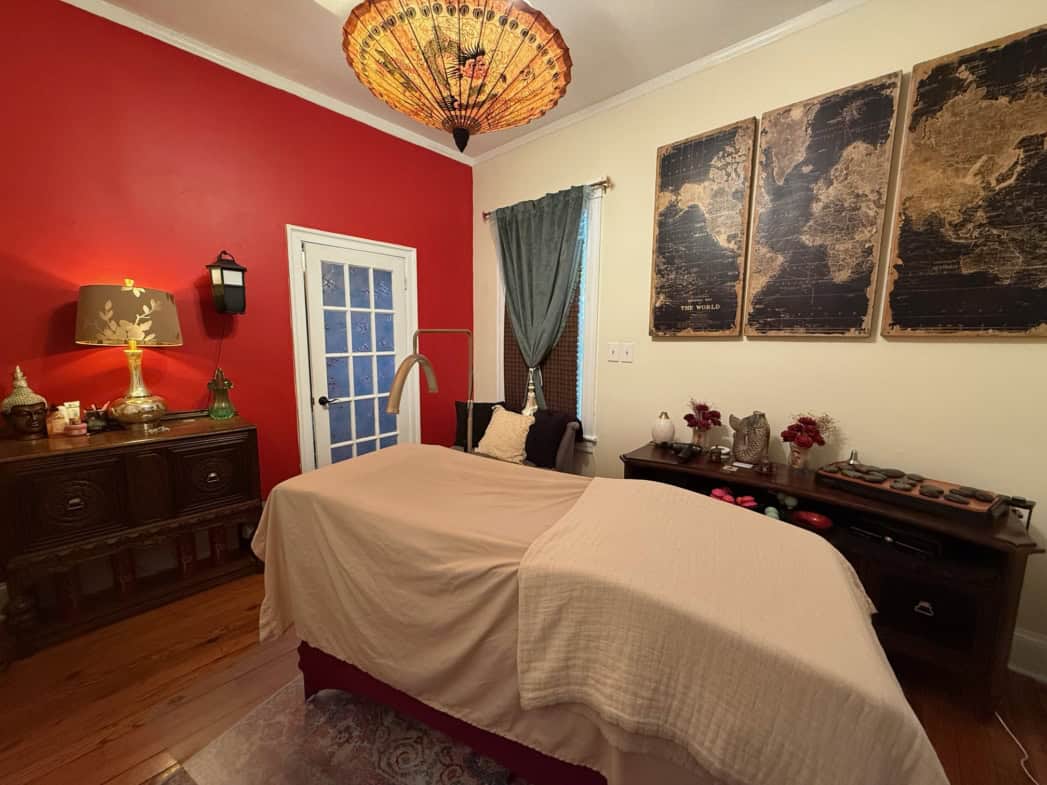Relaxing massage room with massage table, red wall, artwork, and soothing lighting at Salon Renter.