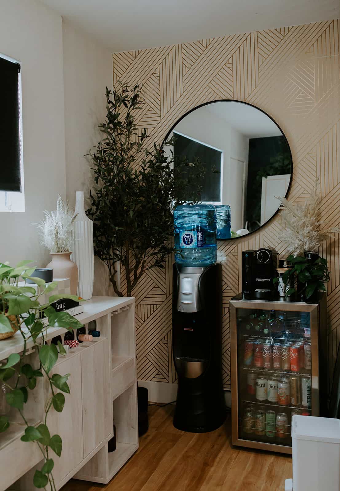 Bright salon space featuring a water cooler, large round mirror, and lush greenery for a welcoming a.