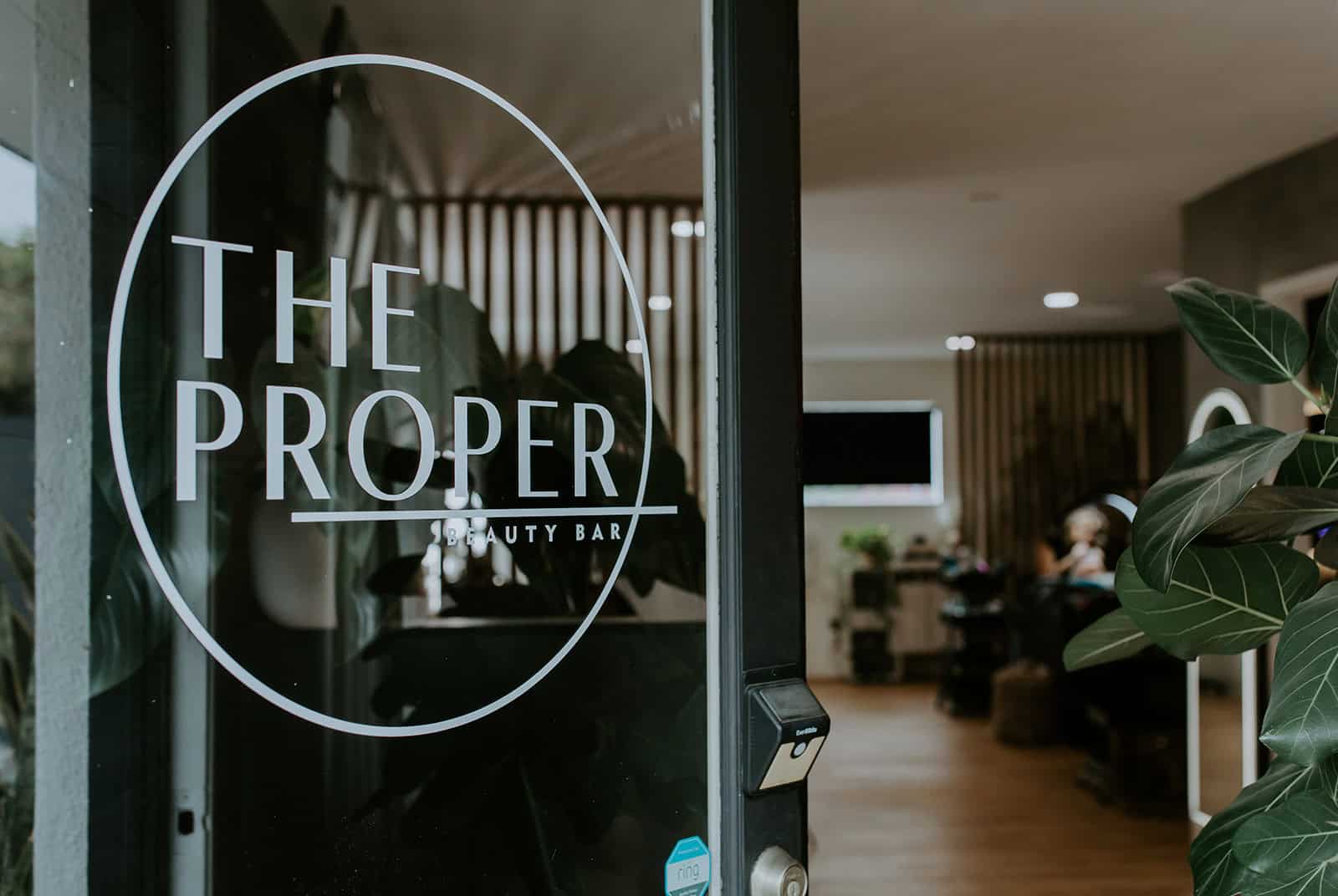Entrance door of The Proper Beauty Bar showcasing modern salon branding.