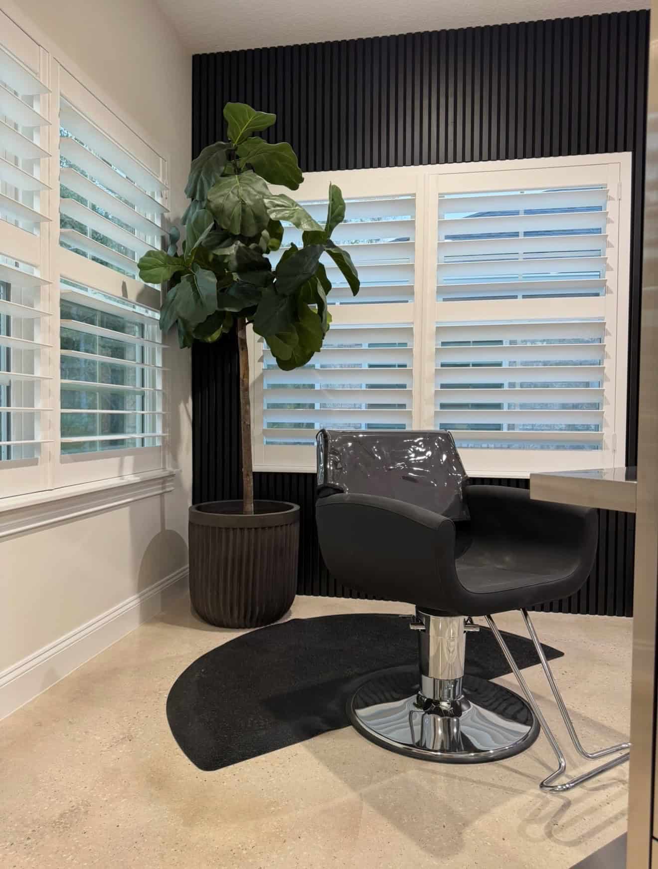 Modern salon styling chair with large potted plant and window shutters in a contemporary salon inter.