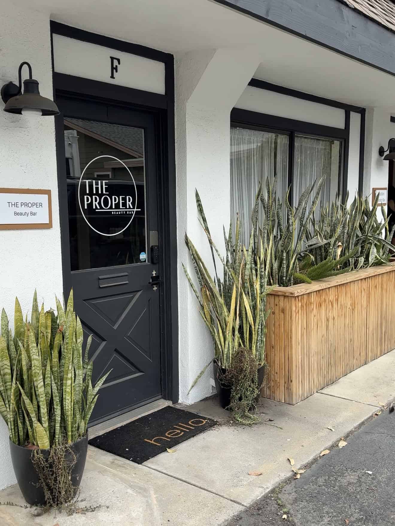 Entrance door of The Proper Beauty Bar with plants and modern design.
