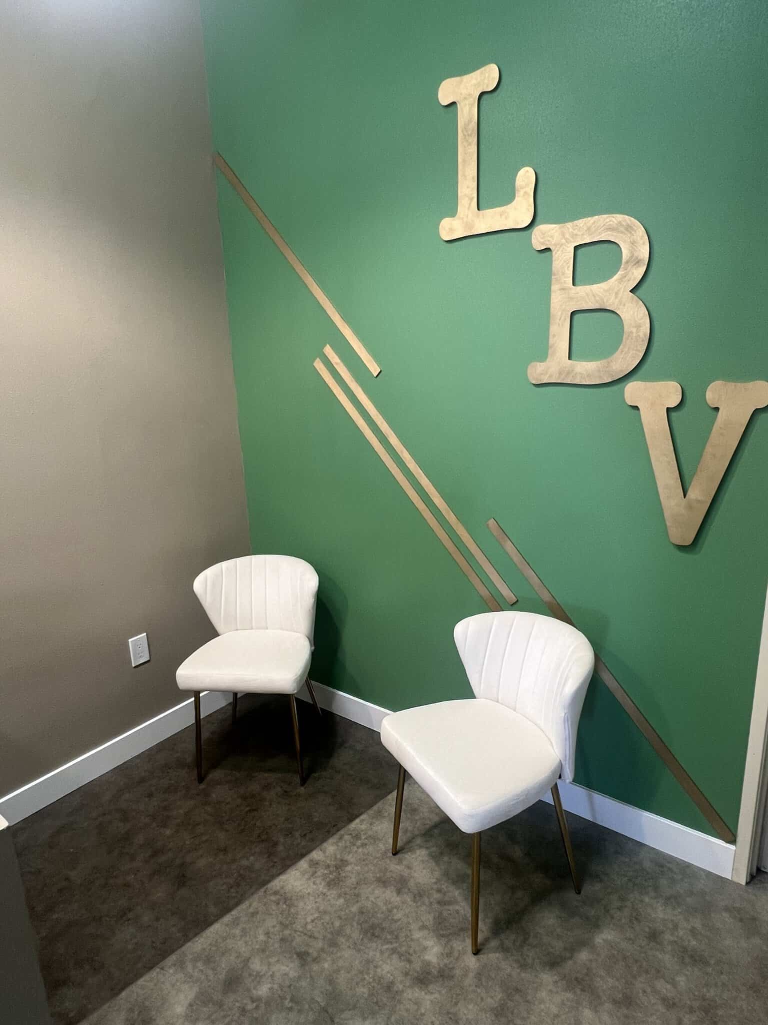 Stylish salon waiting area with two white chairs and decorative "LBV" wall art on green accent wall.
