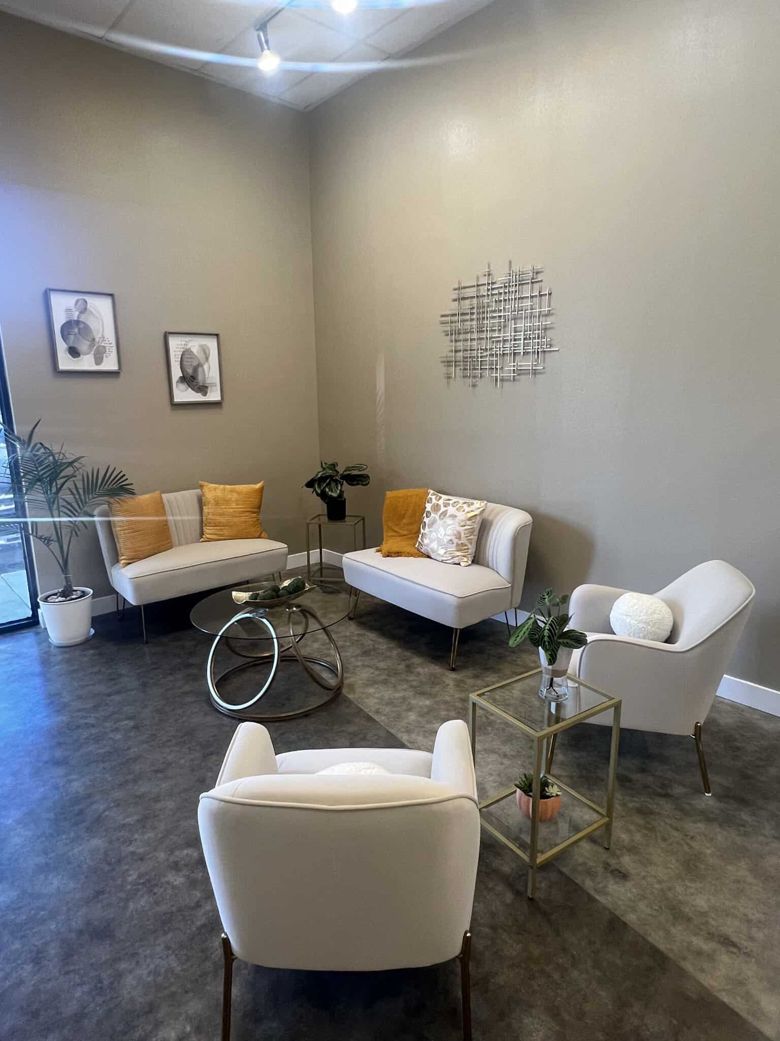 Modern salon waiting area with comfortable chairs, artwork, and plants for a welcoming atmosphere.