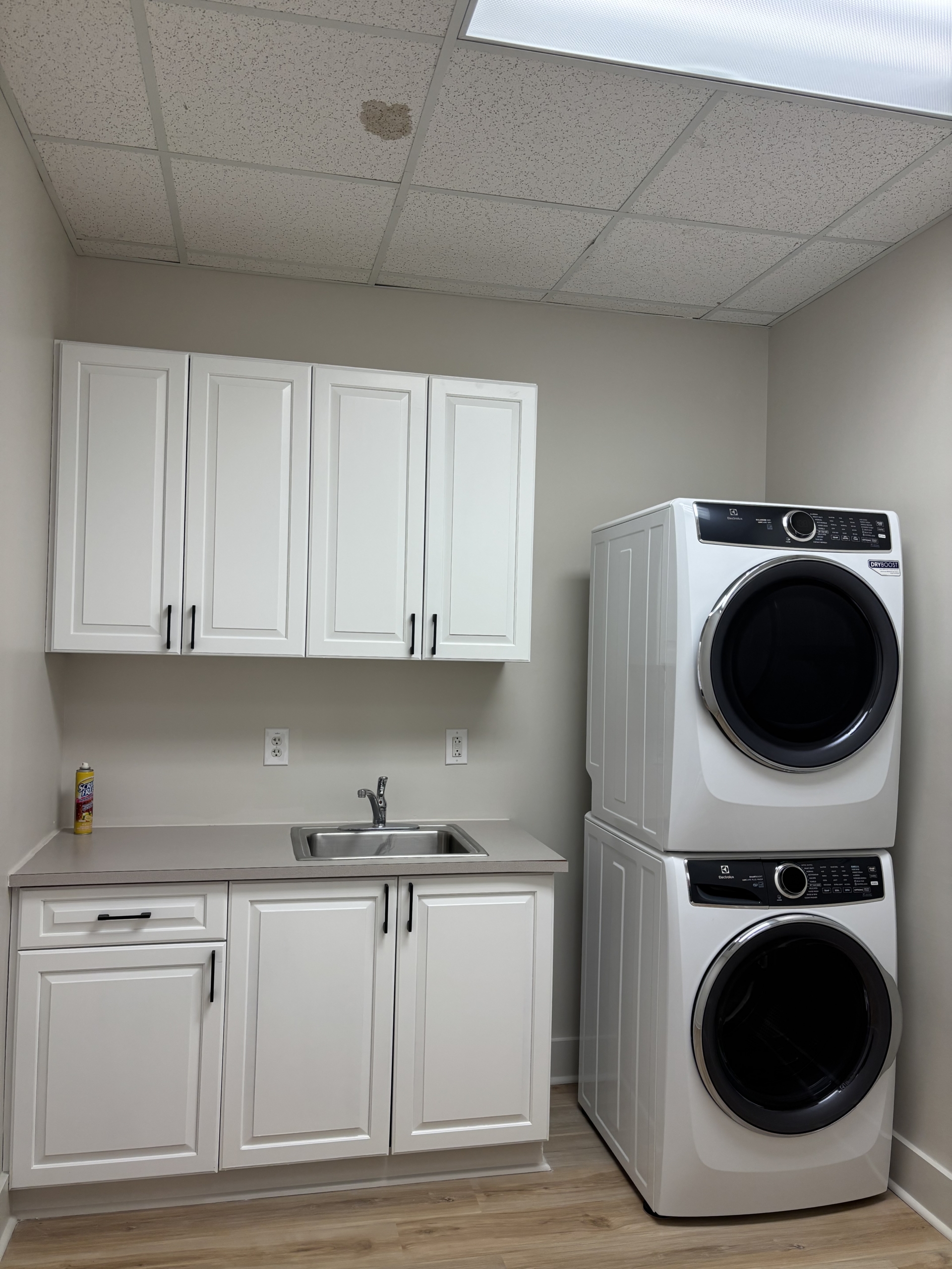 Laundry room with stacked washer and dryer, white cabinets, and sink.