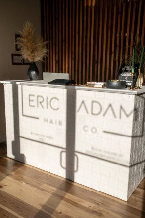 Stylish salon reception area featuring a white tiled desk, decorative vase, and wood-paneled wall.