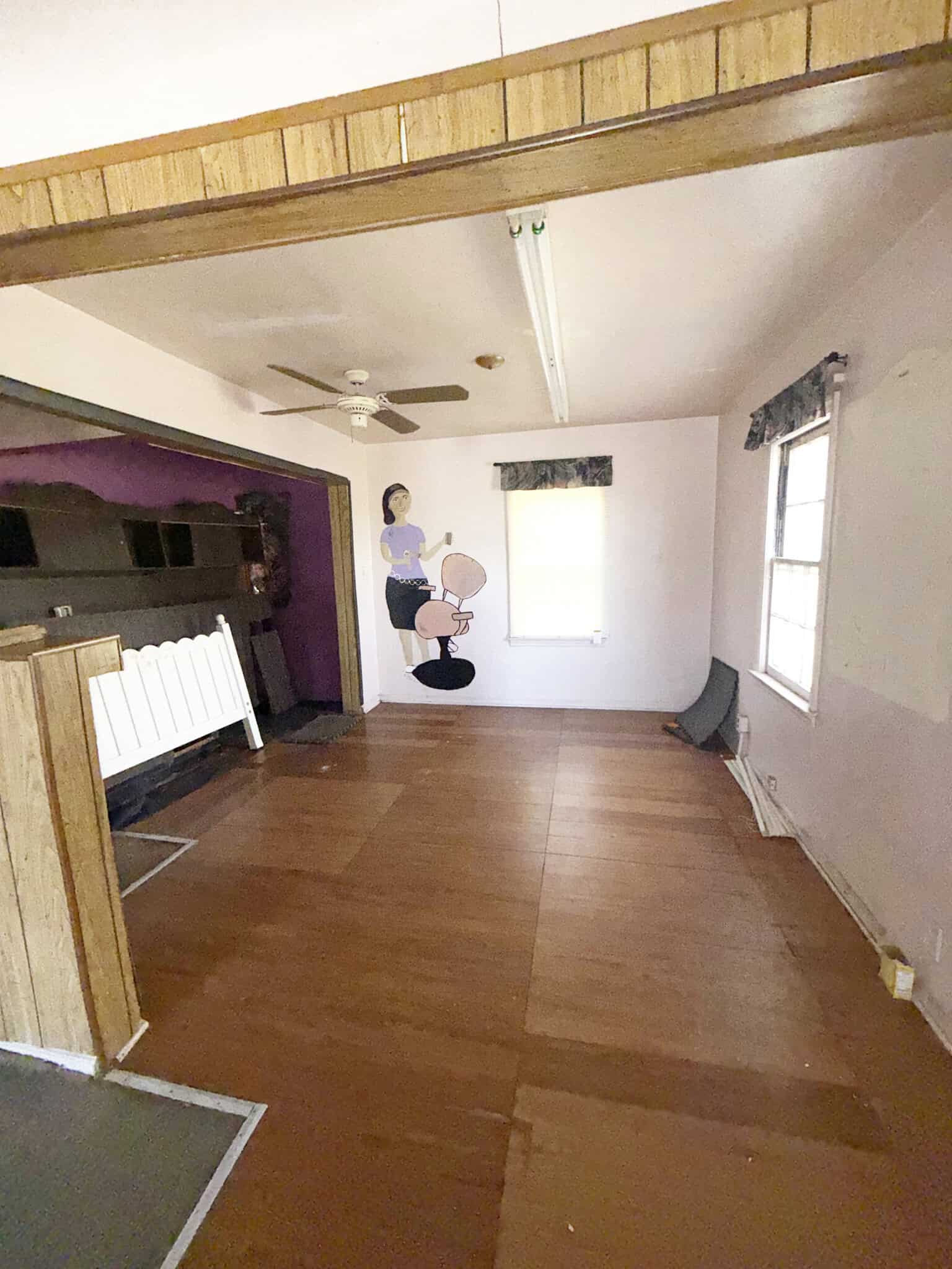 Empty salon studio with wooden floors, large windows, and a wall mural of a woman getting a haircut.
