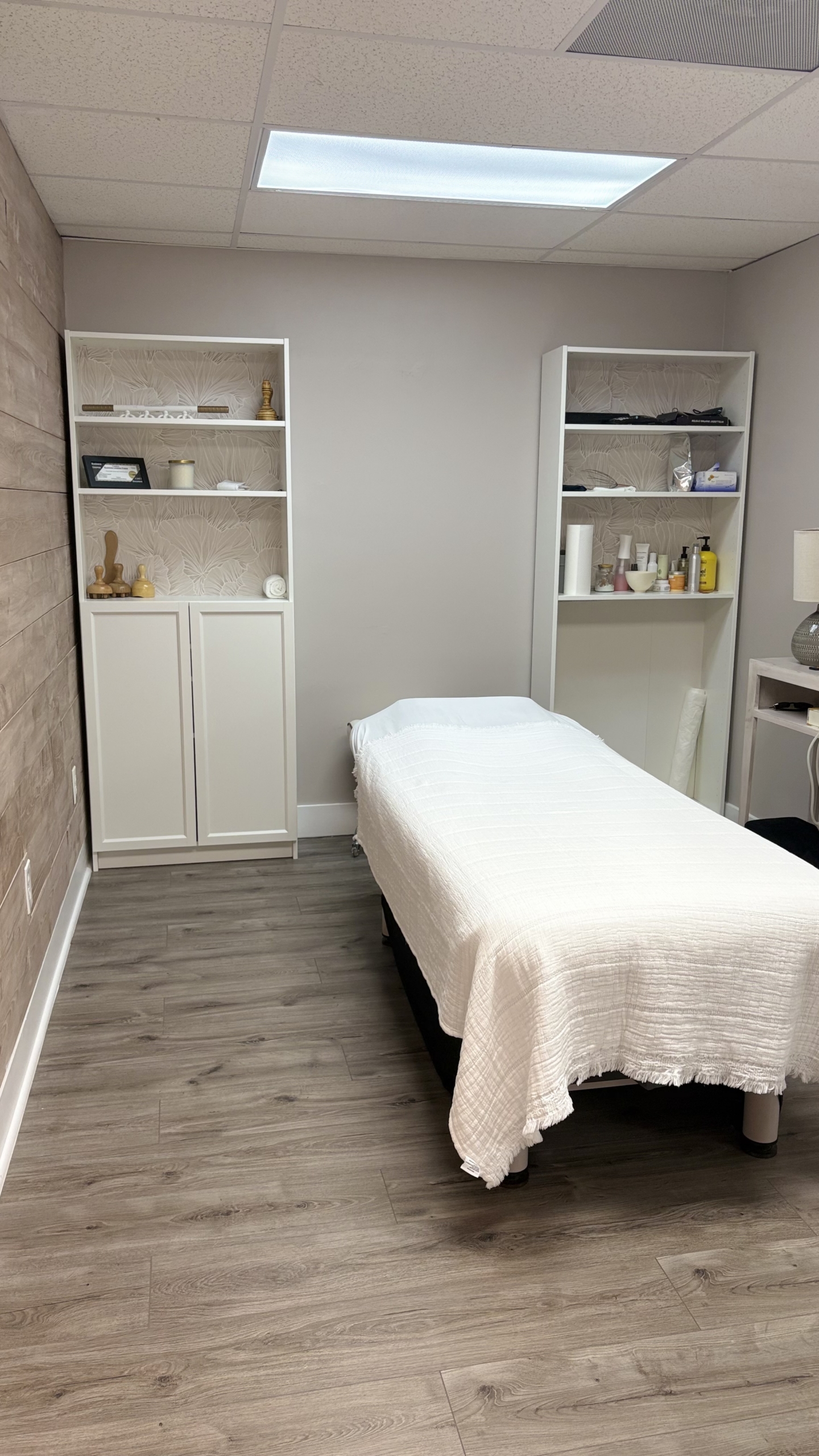 Clean and organized spa treatment room with massage bed and shelves.