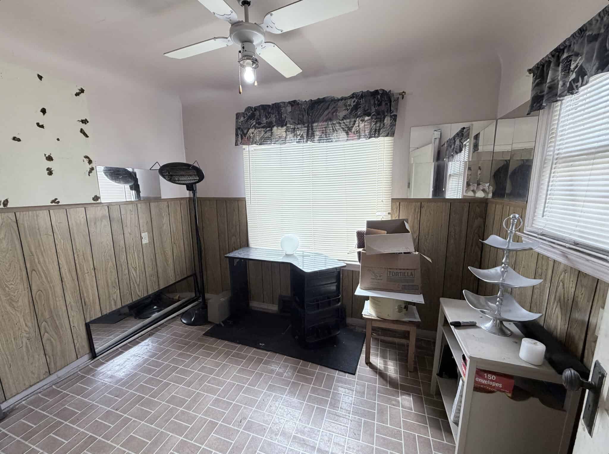Small salon room with wooden wall paneling, window blinds, and a desk for styling or consultations.