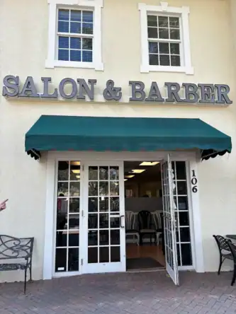 Exterior view of a salon and barber shop with a green awning and open glass door.